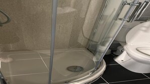 Una ducha con puerta de vidrio, un inodoro y suelo de baldosas.
