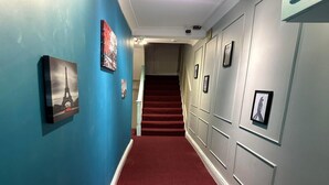Un pasillo con alfombra roja, paredes azules y una escalera que sube a otro piso.