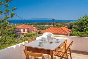 Eine Terrasse mit Tisch für zwei Personen, mit Blick auf eine Küstenlandschaft mit Häusern und blauem Himmel.