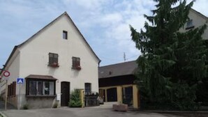 A two-story building with a gabled roof, a small porch, and a visible entrance.