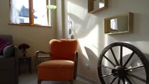 A room with a large wooden wheel, a small table with a vase, and a chair.
