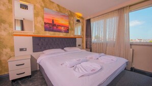 Quarto de hotel com cama, mesa de cabeceira, espelho, quadro e janela com cortinas.