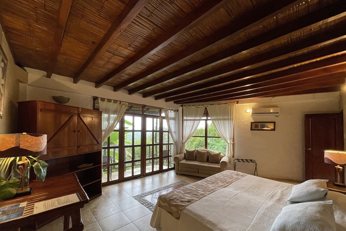 Quarto com cama, escrivaninha, sofá e janela com cortinas.