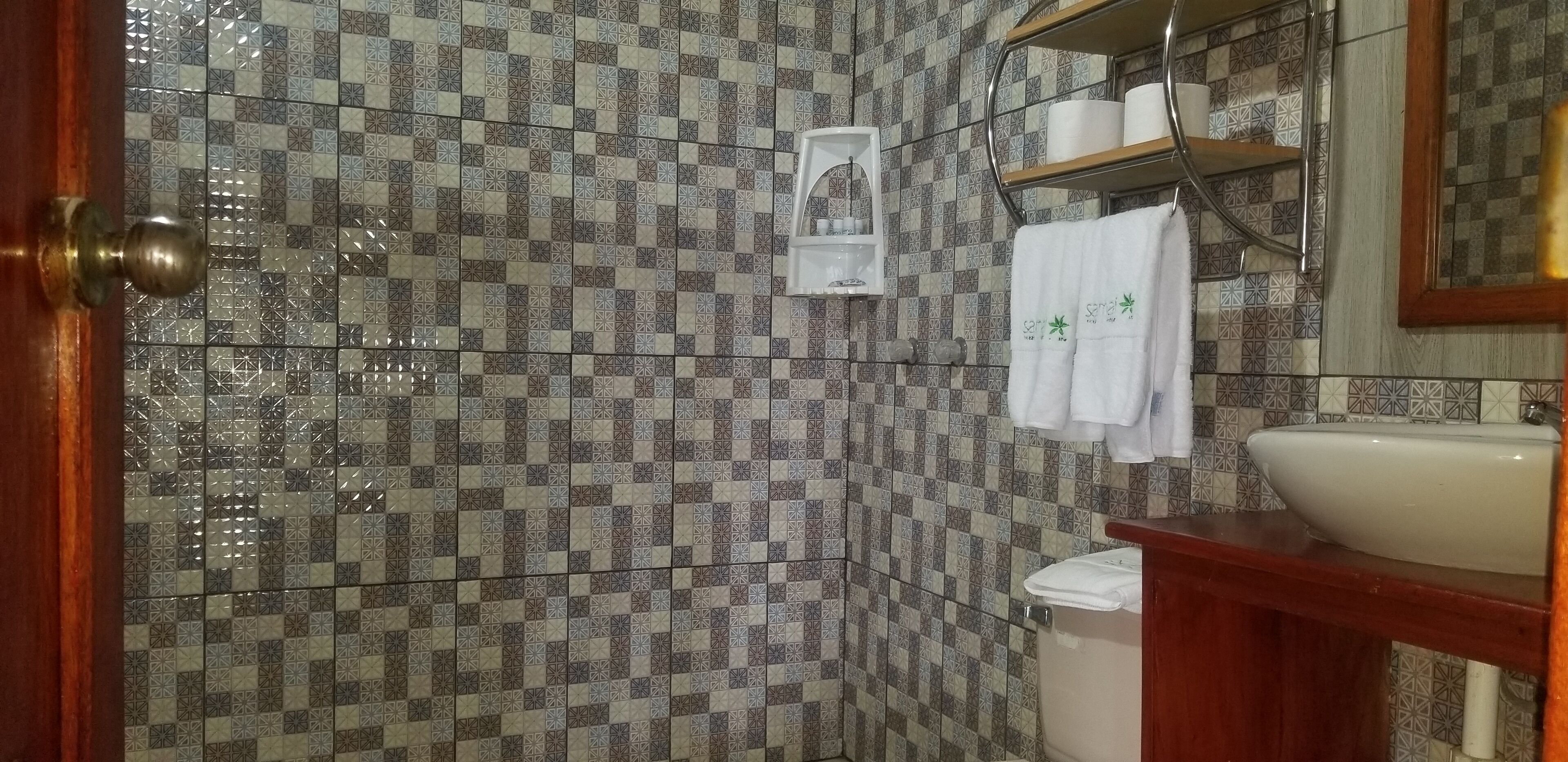 A bathroom with patterned tiles, a sink, a mirror, and a towel rack with towels.