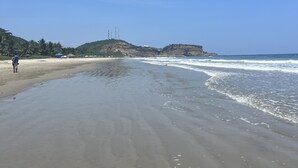 A wide sandy beach with gentle waves, a clear blue sky, and distant hills.