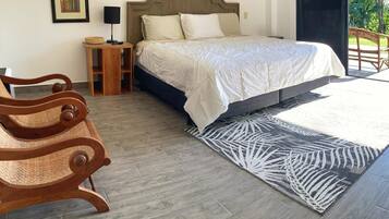 A bedroom with a bed, wooden nightstands, a woven chair, a patterned rug, and a framed picture on the wall.