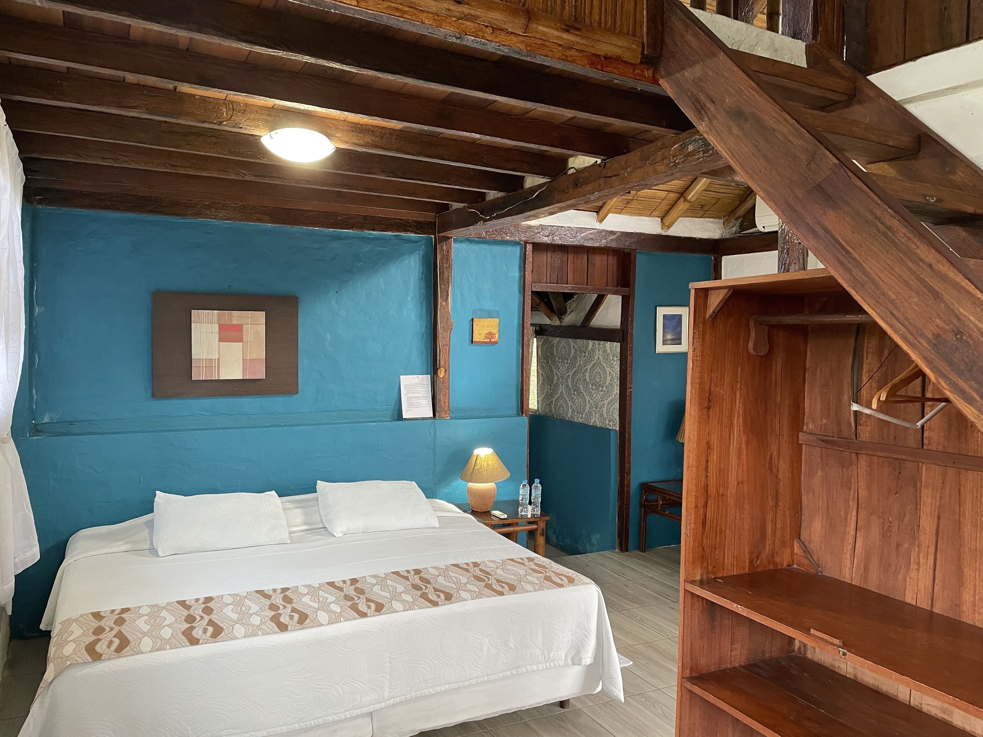 A bedroom with a bed, a wooden wardrobe, and a blue wall.