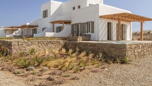 Uma villa moderna branca com um muro de pedra, área de estar ao ar livre e piscina.