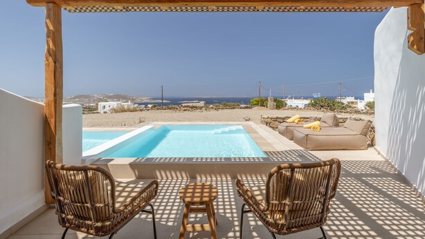 Uma área de piscina com duas cadeiras de vime e uma mesa, com vista para a praia e o mar.