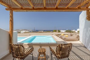A pool area with two wicker chairs and a table, overlooking a beach and the sea. - Aya Sofia Suites (Mykonos)