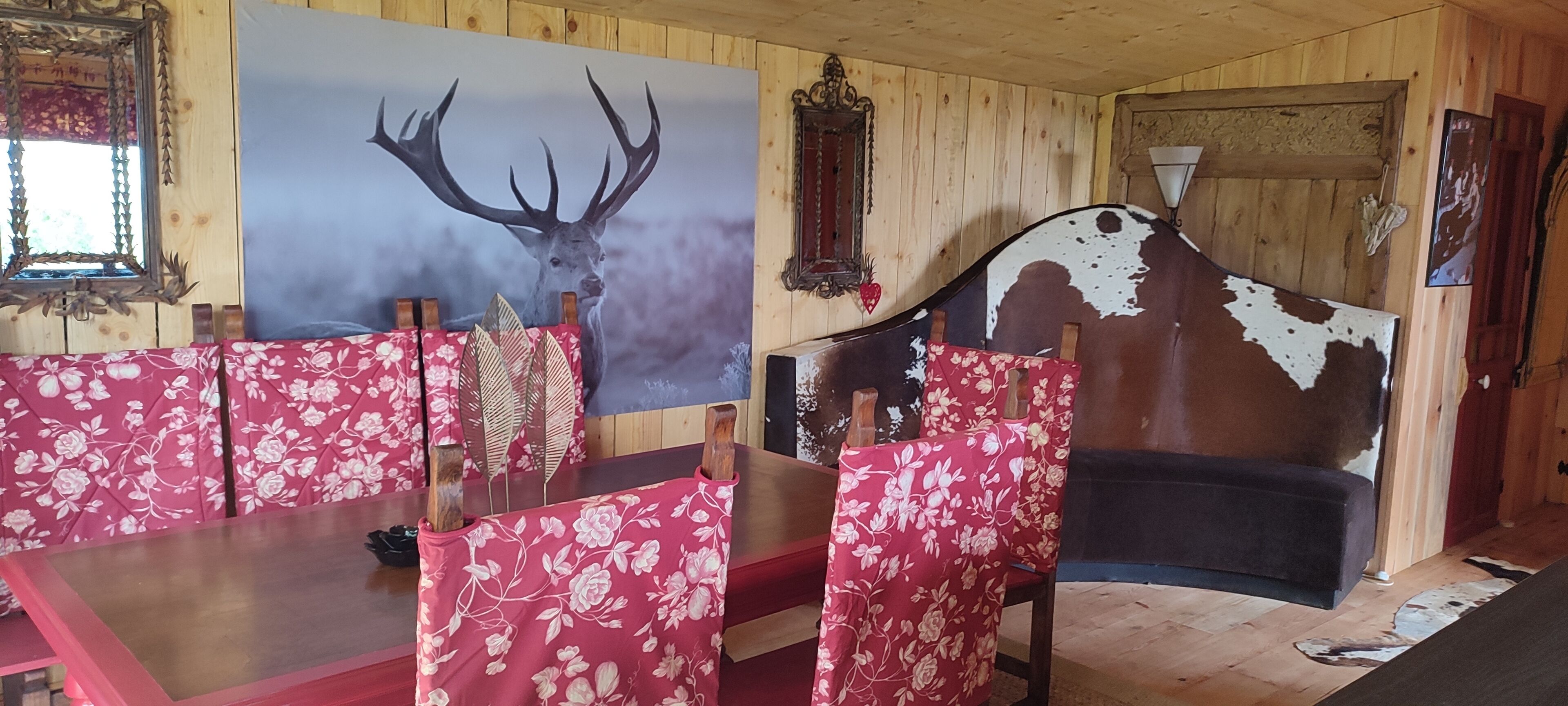 Een rustiek interieur met houten wanden, een groot hert schilderij, een uniek gehouwen hoofdbord en meubels met bloemenmotief.