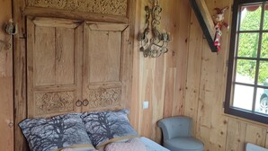 Ein Zimmer aus Holz mit einem Bett, einem Sessel und einem Fenster.