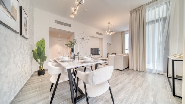 A modern dining area with a white table, black chairs, and a potted plant. - Exquisite 2BR w/ Assistant’s Room at Mesk 1 Midtown Dubai Production City by Deluxe Holiday Homes (Dubai)