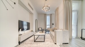 A modern living room with a flat-screen TV, a coffee table, a sofa, and a chandelier. - Exquisite 2BR w/ Assistant’s Room at Mesk 1 Midtown Dubai Production City by Deluxe Holiday Homes (Dubai)