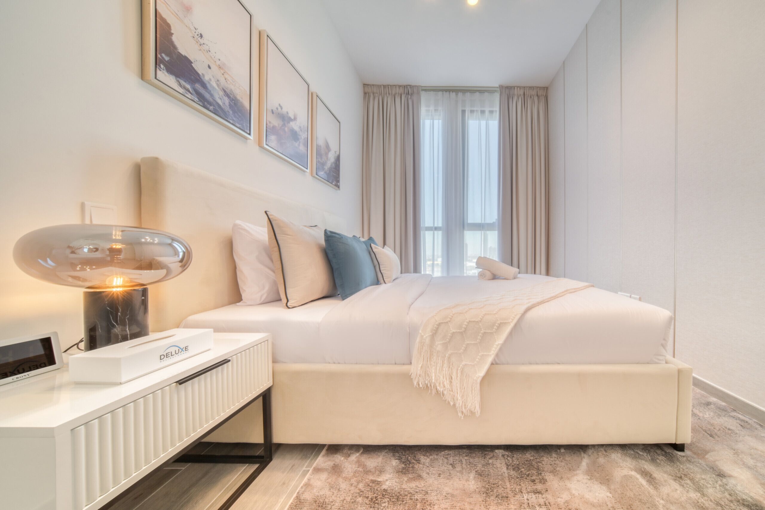 Un dormitorio moderno con cama, mesita de noche, lámpara y una obra de arte en la pared.