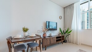A modern living room with a dining table, chairs, a TV, and a large window with curtains. - Canal View, Walking Distance to Bay Avenue Mall, Mins to Downtown Dubai (Dubai)