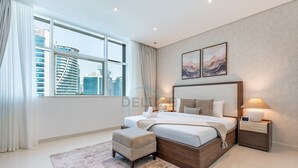 A modern bedroom with a large bed, bedside tables, a view of the city, and artwork on the wall. - Canal View, Walking Distance to Bay Avenue Mall, Mins to Downtown Dubai (Dubai)