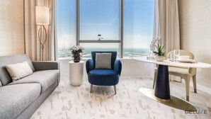 A modern hotel room with a large window, a grey sofa, a blue armchair, a round table with a white bowl, and a potted plant. - Heavenly Studio at The Palm Tower Palm Jumeirah by Deluxe Holiday Homes (Dubai)