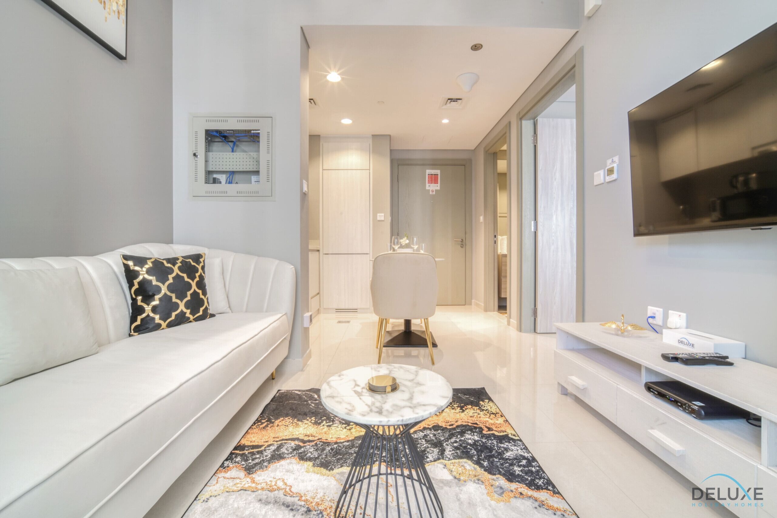 A modern living room with a white sofa, a marble coffee table, and a TV on the wall.