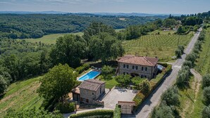 Una villa in pietra con piscina, circondata da vegetazione lussureggiante e vigneti.