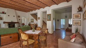 Un ampio soggiorno con camino, divano verde, tavolo da pranzo con sedie e una scala che conduce in un'altra stanza.