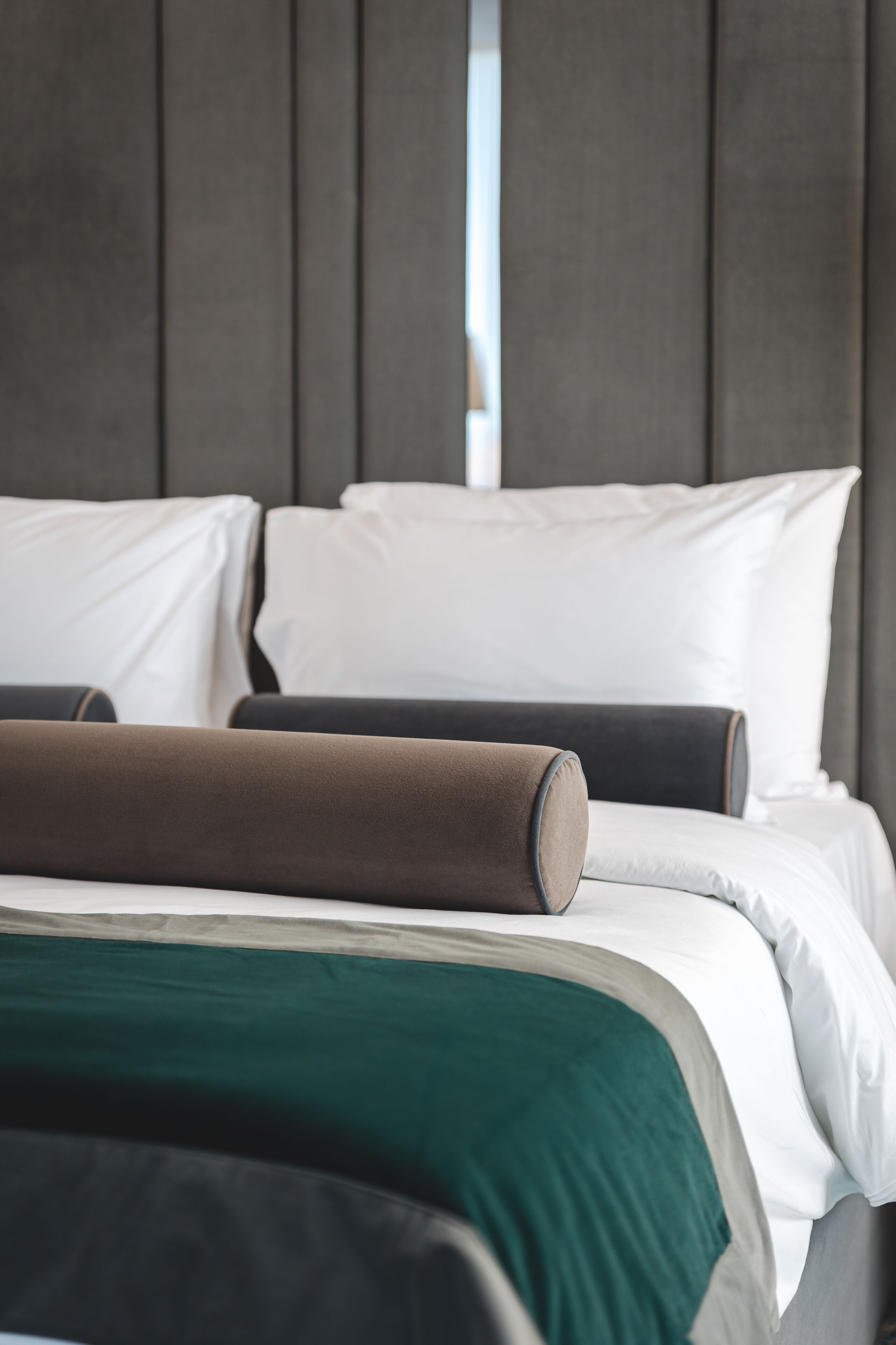 Una cama bien hecha con almohadas blancas y marrones, una manta verde y un cabecero oscuro.