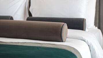 Una cama bien hecha con almohadas blancas y marrones, una manta verde y un cabecero oscuro.