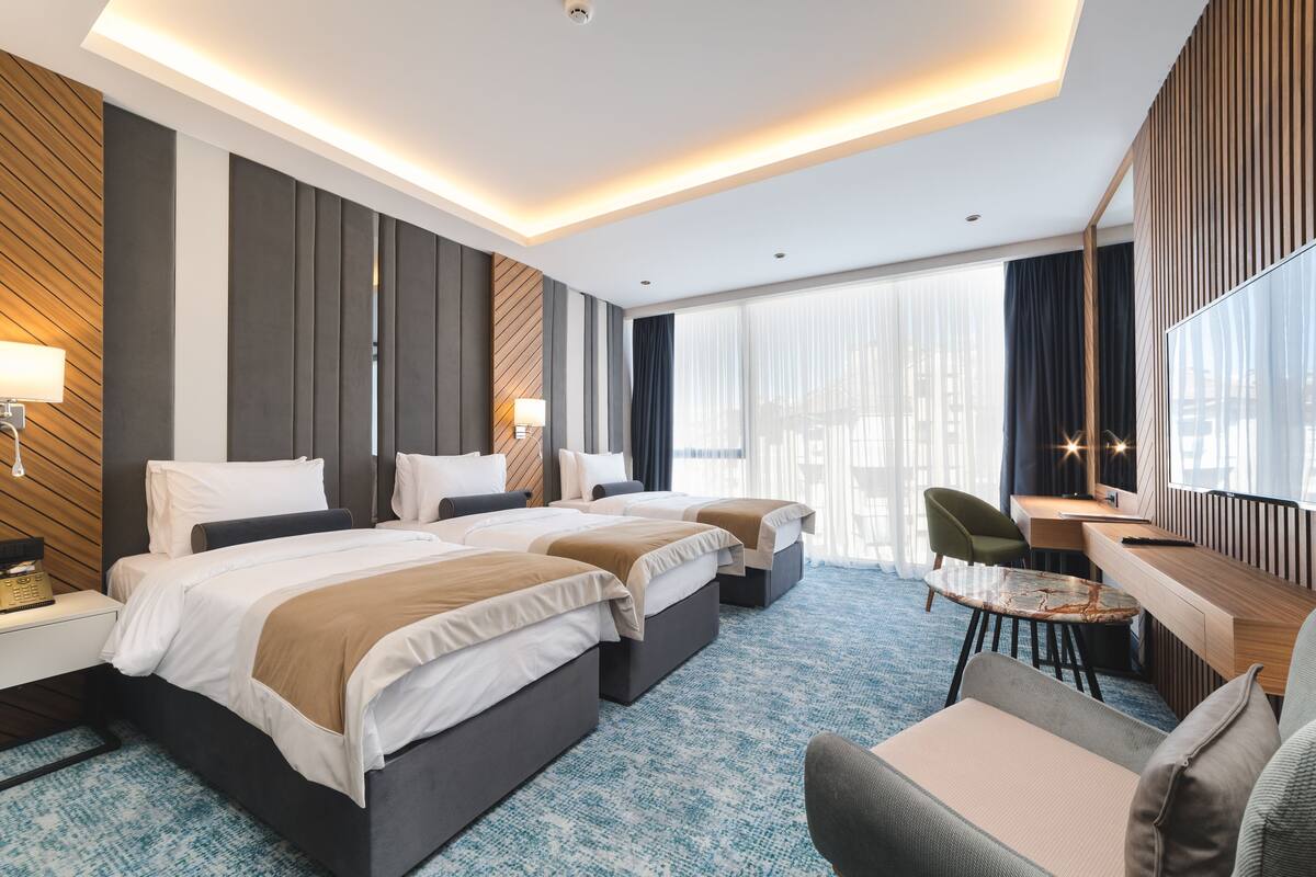 Una habitación de hotel moderna con dos camas, un escritorio, una silla y un ventanal con cortinas.
