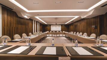 A conference room with long tables, chairs, water bottles, and a projector screen.