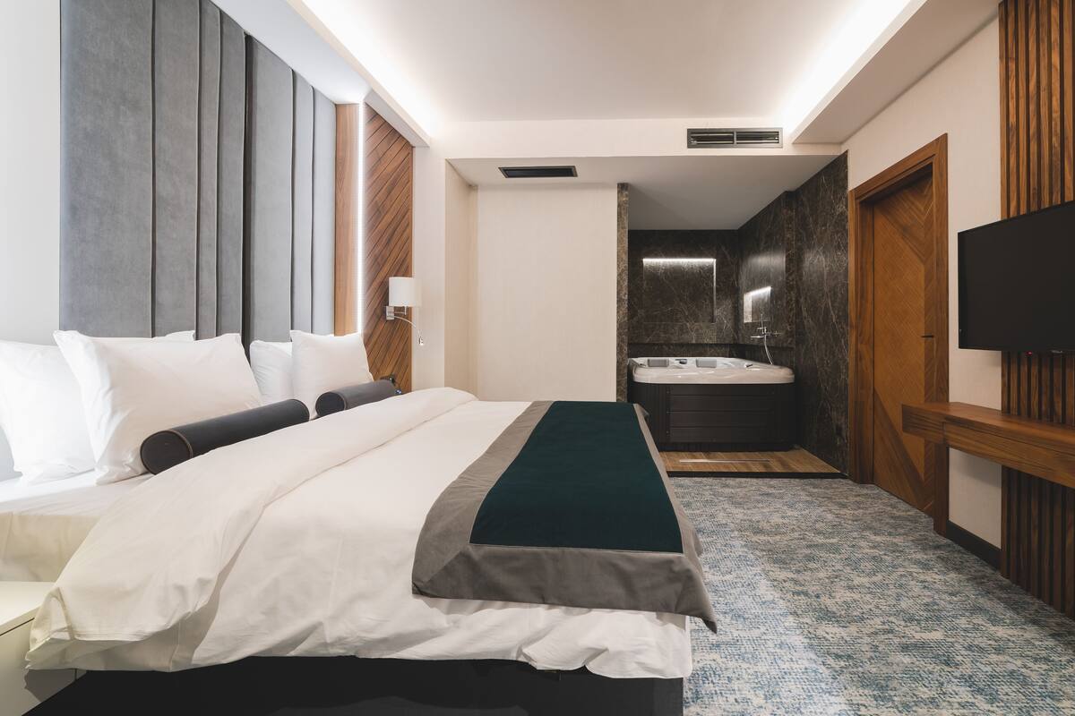 Habitación de hotel con cama, televisión, baño con bañera y pared de paneles de madera.