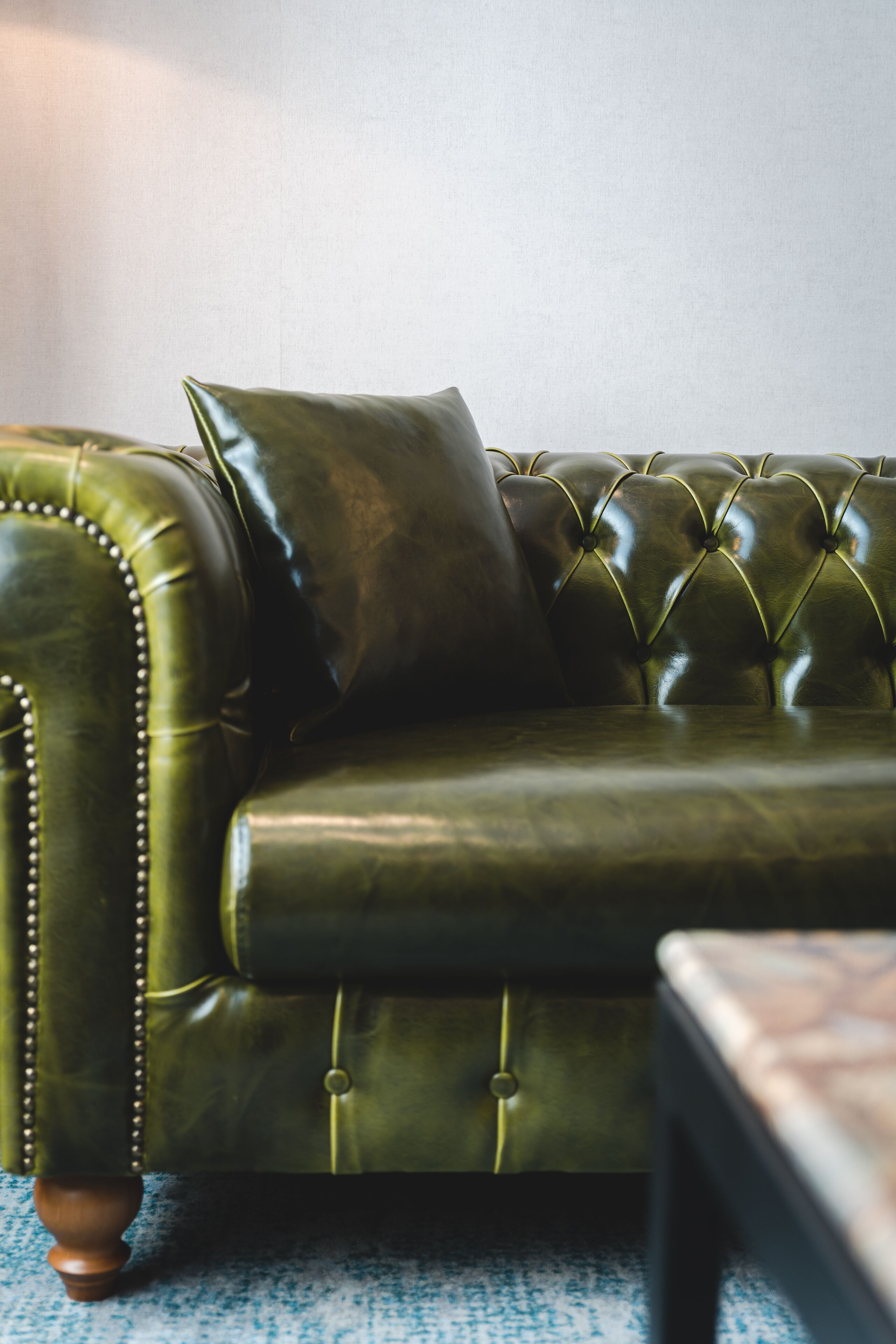 A green leather sofa with a tufted backrest and wooden legs.