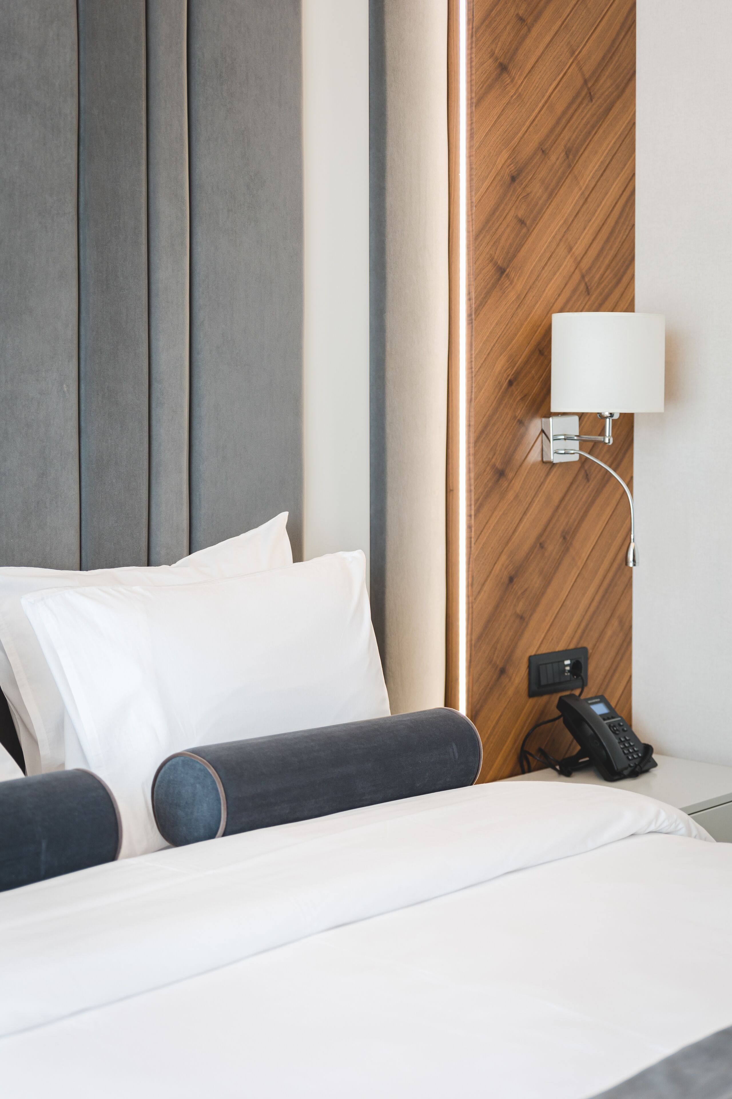 A hotel room with a bed, pillows, a bedside lamp, and a phone on the nightstand.