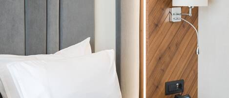 Una habitación de hotel con cama, almohadas, una lámpara de noche y un teléfono en la mesita.