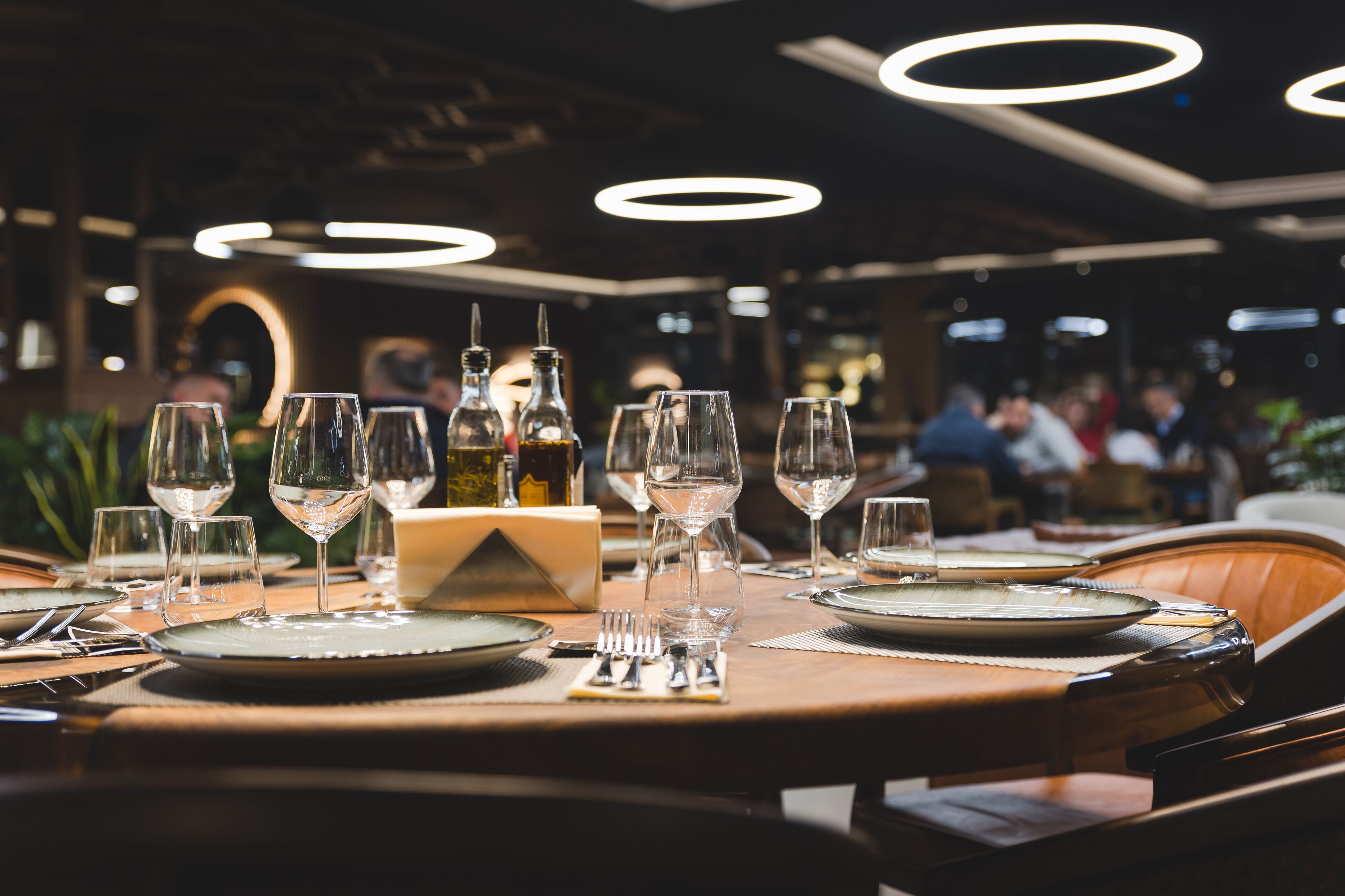 A restaurant table set with wine glasses, plates, and cutlery, with a bottle of wine and a menu on the table.