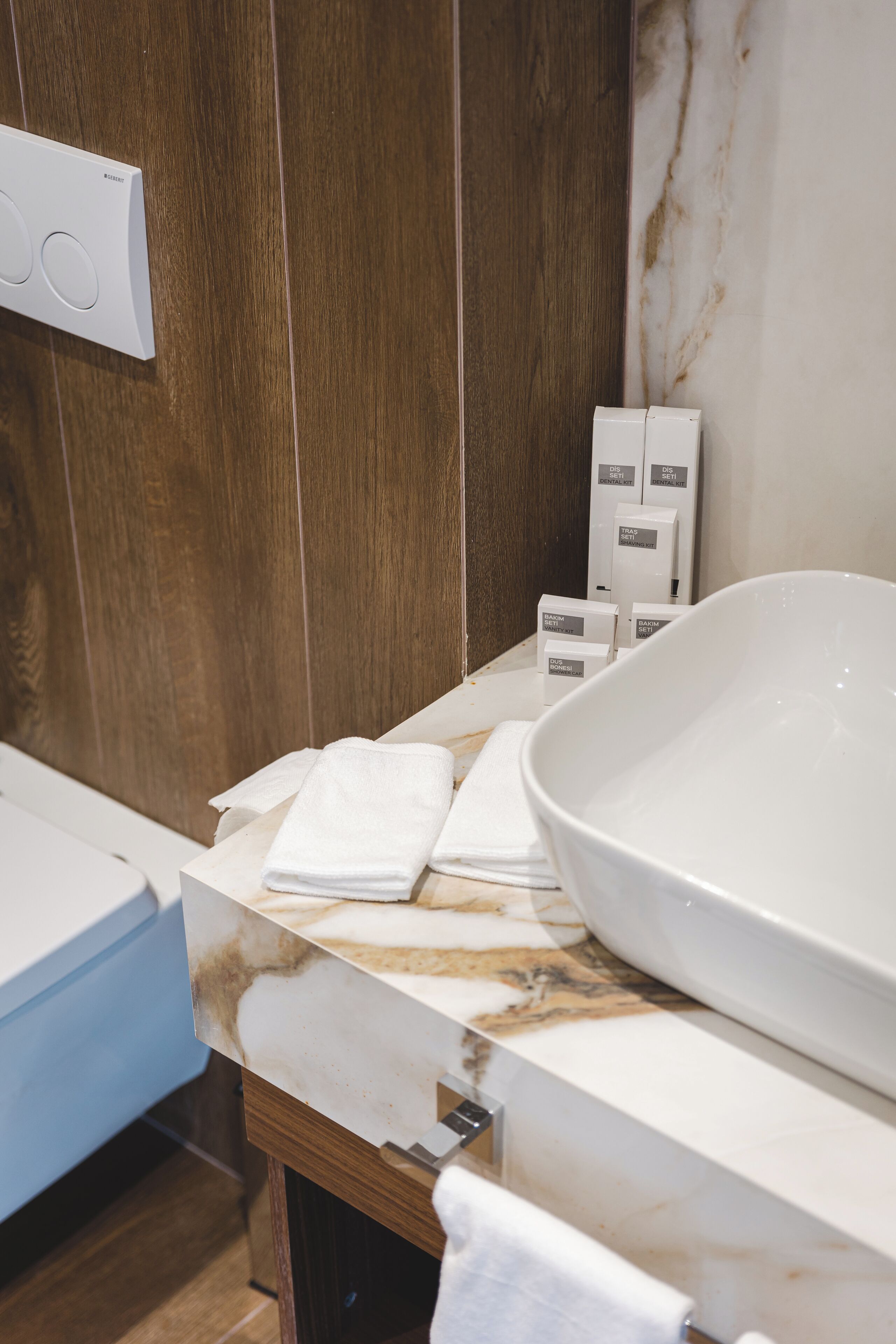 A bathroom with a large white sink, wooden panel walls, and a marble countertop.
