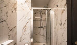 A modern bathroom with a glass-enclosed shower, marble walls, and a white toilet. - Spinola Stays  (St. Julian's)