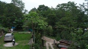 A rural setting with a paved path leading through a lush green area, a parked car, and a motorcycle. - Camp David (Kohima)