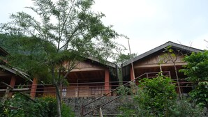 A traditional wooden building with a stone wall and a staircase leading to a wooden deck. - Camp David (Kohima)