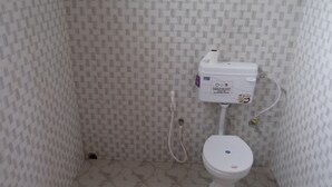 A small, tiled bathroom with a toilet, a wall-mounted bidet, and a toilet paper holder. - Camp David (Kohima)