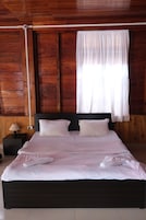 Una cama bien hecha con sábanas y almohadas blancas, un cabecero de madera y una mesita de noche con lámpara.
