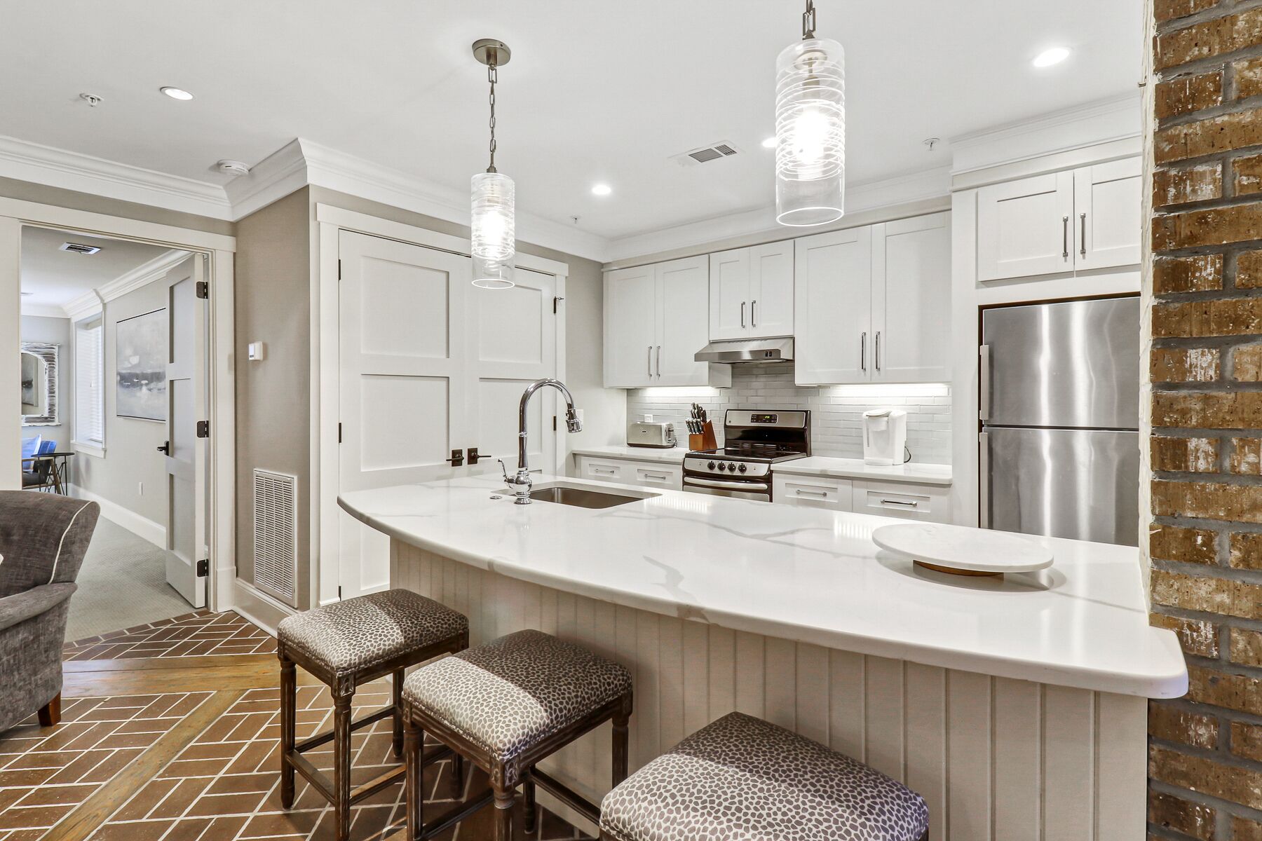 A modern kitchen with white cabinetry, a stainless steel refrigerator, and a large island with stools.