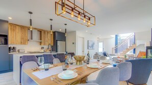 A modern kitchen with wooden cabinets, a dining area with a long table set for six, and a staircase leading to an upper level.