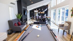 A modern living room with a pool table, grey sofas, and a dining area.