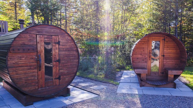 Two wooden sauna cabins with doors, set on a gravel path in a forested area.