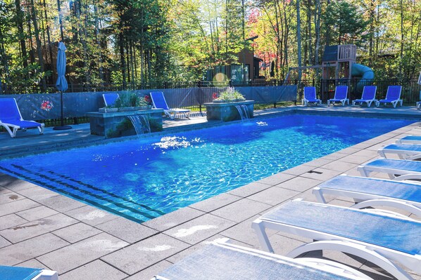 Ein Swimmingpool mit klarem, blauem Wasser, umgeben von Liegestühlen und einem kleinen Wasserfall.