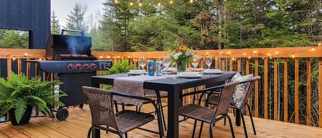 An outdoor deck with a grill, dining table, chairs, and string lights.