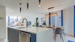 A modern kitchen with a central island, stainless steel dishwasher, and pendant lighting.