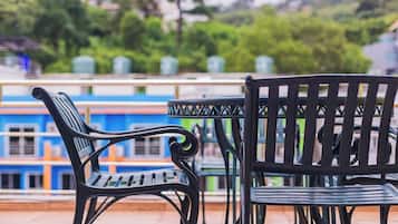 A terrace with two black metal chairs and a table, overlooking a blue building and greenery.