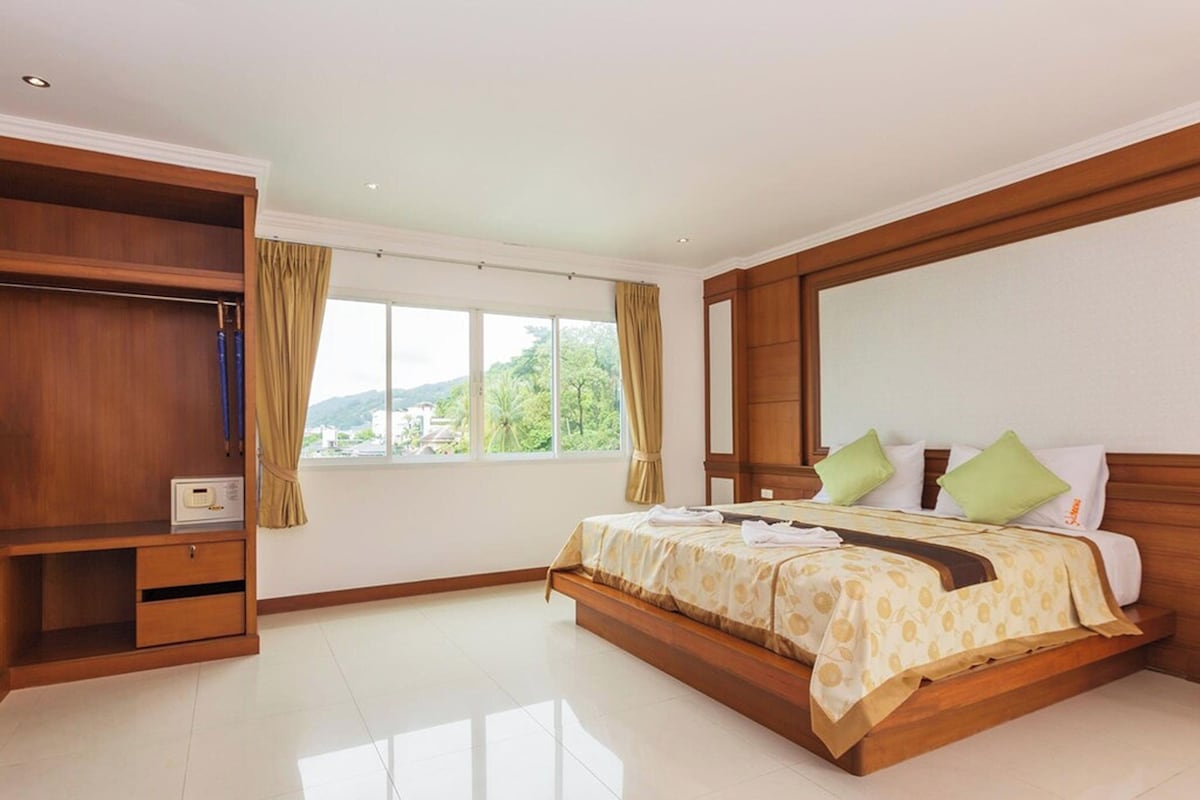 A bedroom with a bed, a wardrobe, a window with curtains, and a view of greenery.