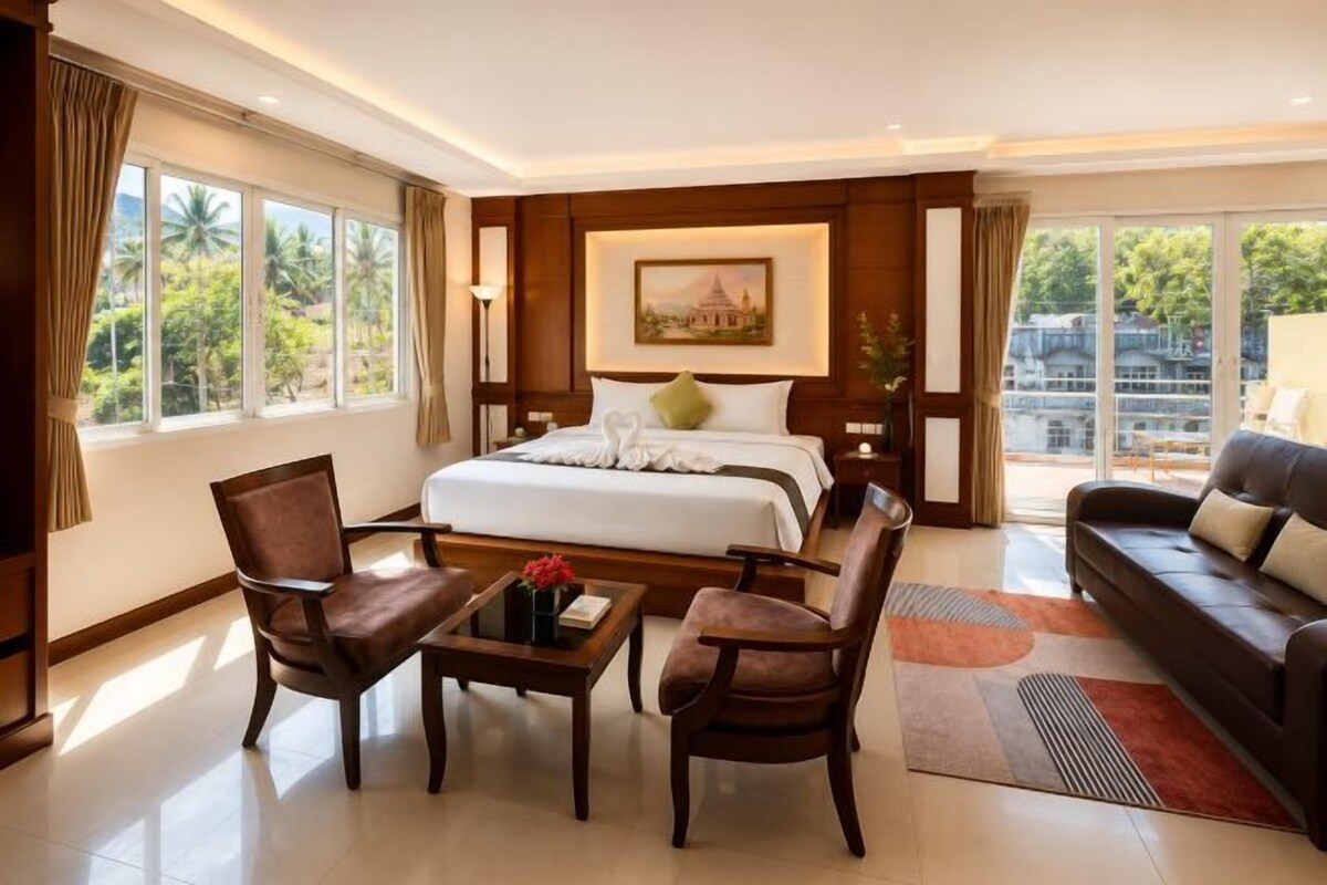 A hotel room with a large bed, a sofa, a coffee table, and a view of the outdoors.